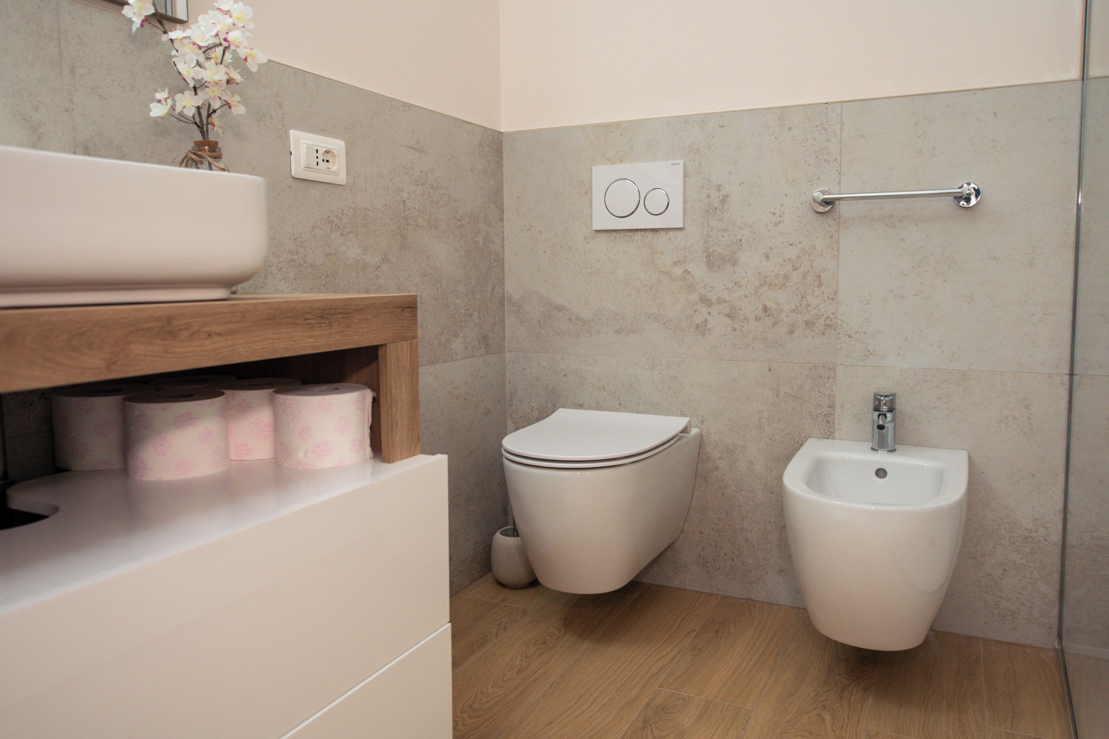 A bathroom with a toilet, bidet, and a shelf with toilet paper.