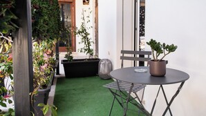 Un pequeño espacio al aire libre con mesa y sillas, rodeado de plantas en macetas y césped artificial verde.