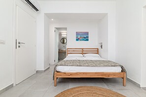 Quarto com cama de madeira, espelho redondo, pintura e banheiro pequeno com pia.