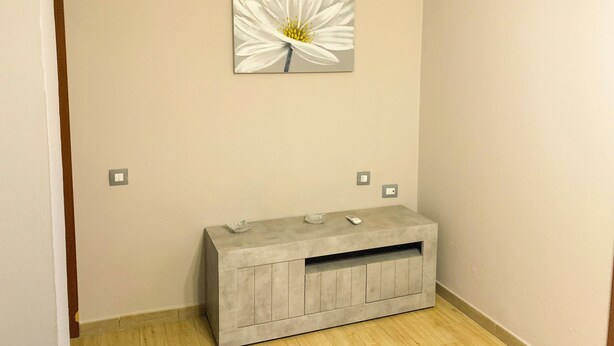 Una habitación con una pared color beige, un cuadro de una flor blanca, un armario gris y suelo de madera.