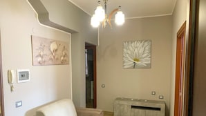 Un salón con sofá, un adorno en la pared, una araña y un radiador.
