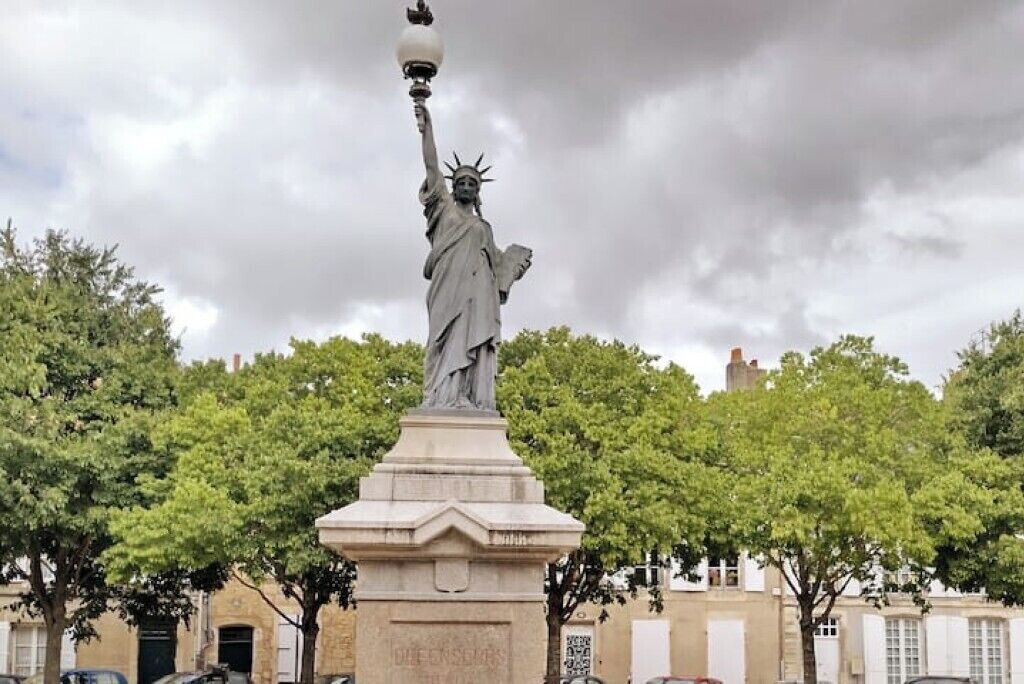 A statue of a figure holding a torch, surrounded by trees and buildings.