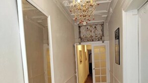 En smal hall med en kristallkrona, en dörr med glaspartier och ett inramat konstverk på väggen.