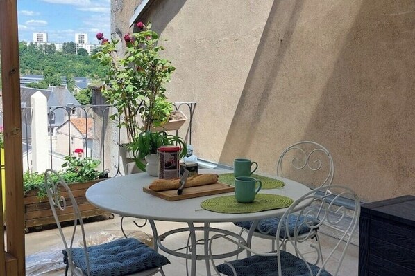 A round table with chairs, a potted plant, a green mug, and a wooden board with a baguette and a knife on a balcony overlooking a cityscape. - Downtown studio apartment with a spacious private terrace—quiet and bright (Poitiers)
