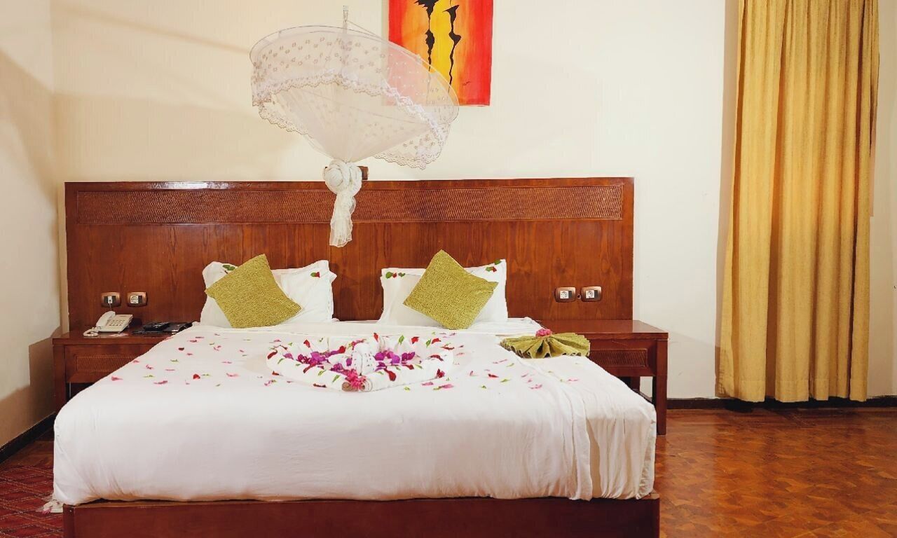 A neatly made bed with a floral bedspread, two pillows, a bedside table with a phone, and a wall art piece.