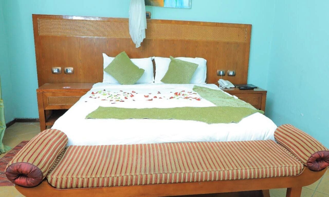 A neatly made bed with a green throw, two pillows, a bedside table with a phone, and a wooden headboard.