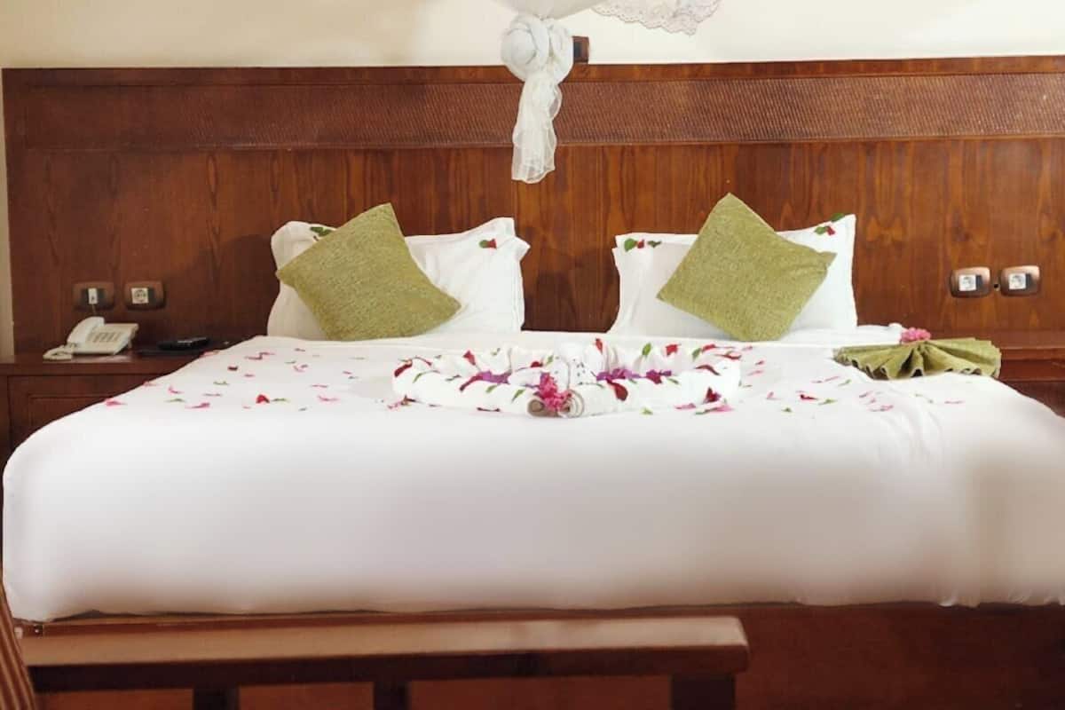 Un letto matrimoniale con copripiumino floreale, due cuscini verdi, una testiera in legno, un comodino con un telefono e un piccolo tavolino con una lampada.