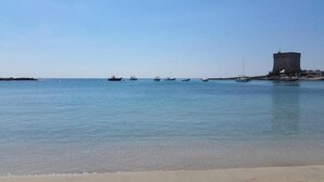 A calm sea with boats, a sandy beach, and a large tower-like structure.