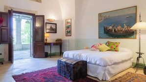 A bedroom with a bed, a desk, a chair, a lamp, and a painting on the wall.
