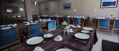A dining area with tables set for service, chairs, and a television on the wall.