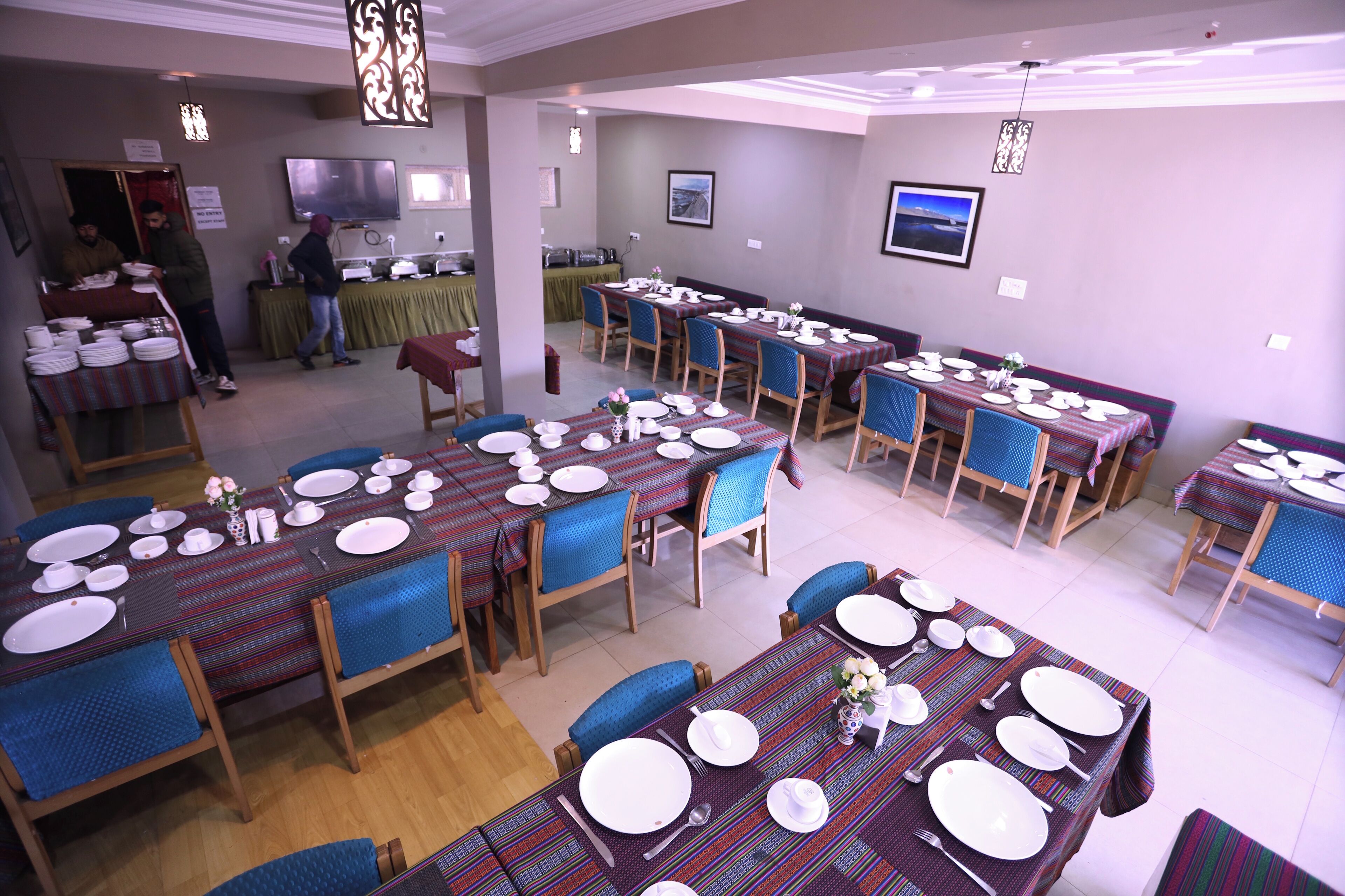 A dining area with multiple tables set for meals, chairs, and a buffet area in the background.