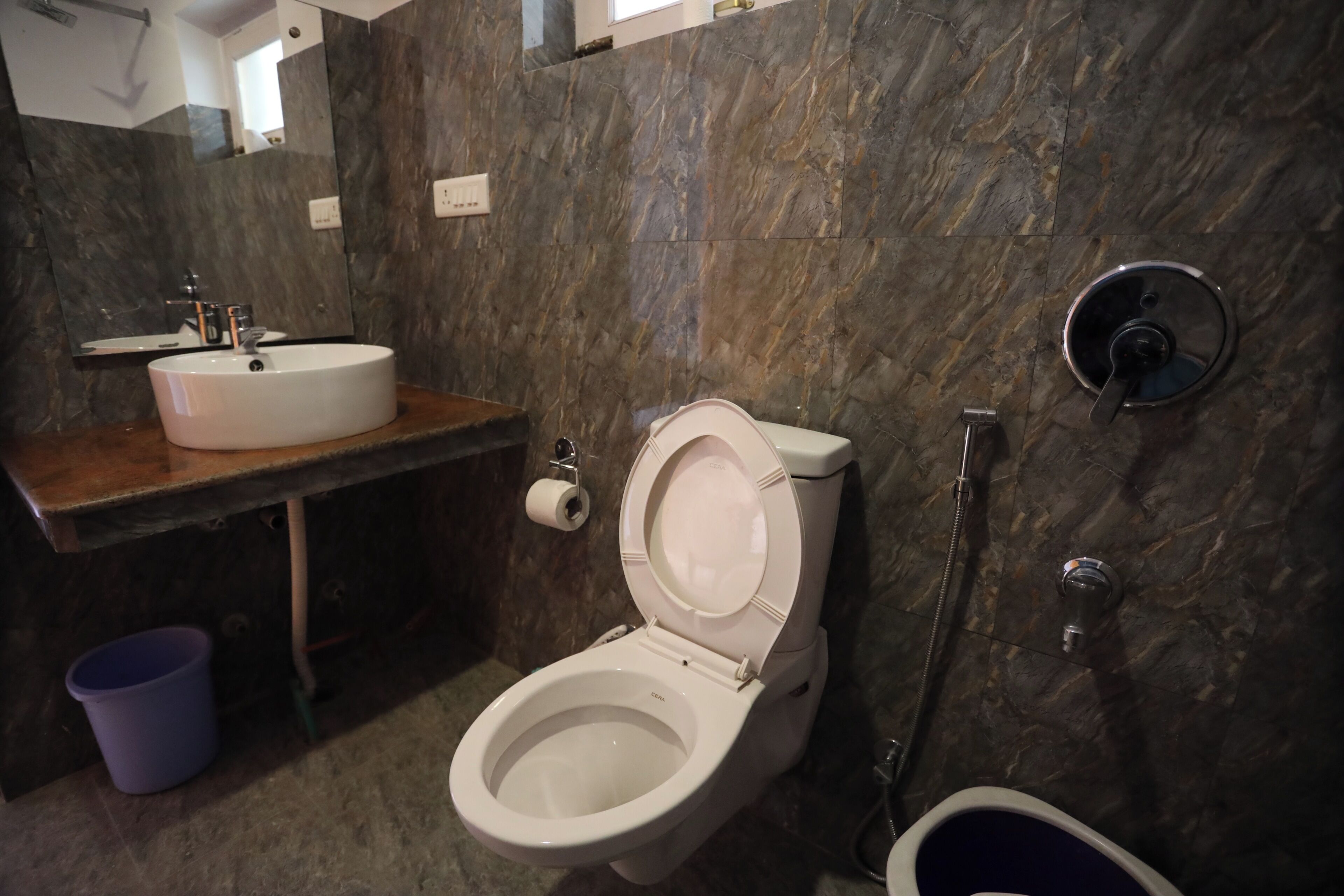 Un baño moderno con pared de mármol, lavamanos blanco, inodoro y ducha.