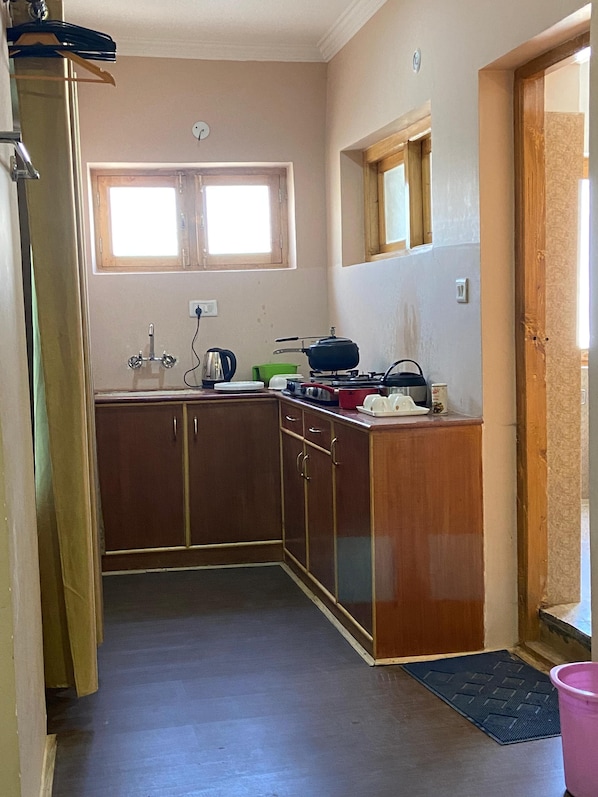 A compact kitchen with wooden cabinets, a gas stove, and a window. - Hotel Latso Ladakh (Leh)