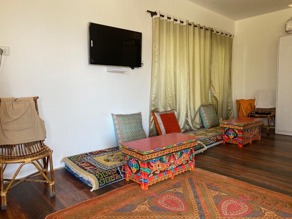 A room with a flat-screen TV mounted on the wall, a sofa with colorful cushions, a patterned rug, and a traditional wooden table. - Hotel Latso Ladakh (Leh)
