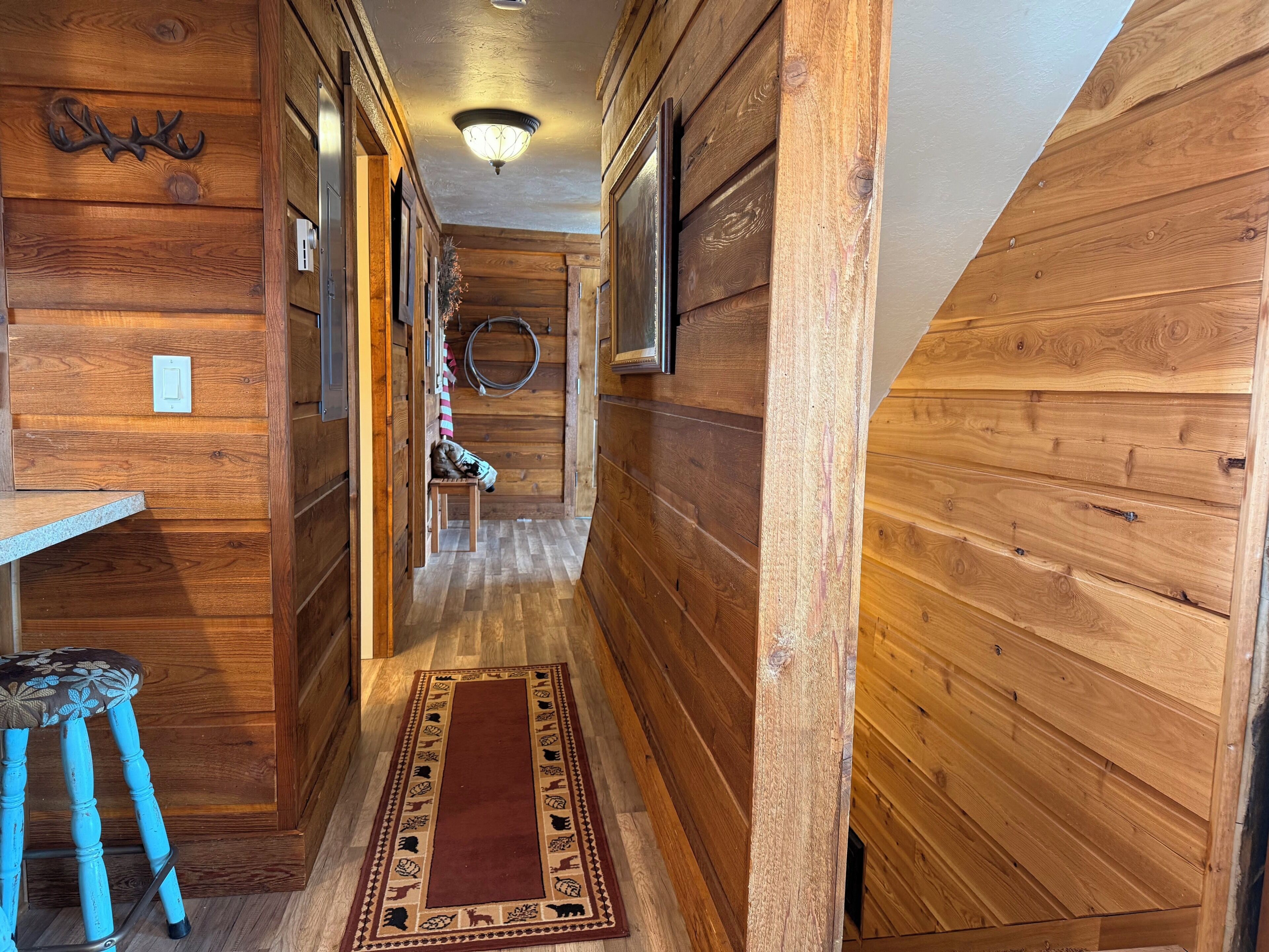 A wooden hallway with a rug, a bench, and a wall-mounted light fixture.