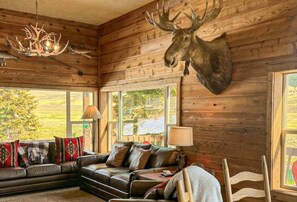Ein Blockhaushaus-Interieur mit Ledersofa, einem aufgehängten Elchgeweih und einer Kandelaber.