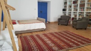 A bedroom with a bed, a bookshelf, a chair, and a patterned rug. - Complete Holiday Home - Herculano, Alexandre and Peregrino (Azóia de Baixo)