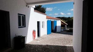 A building with a white exterior, blue doors, and a gravel ground. - Complete Holiday Home - Herculano, Alexandre and Peregrino (Azóia de Baixo)