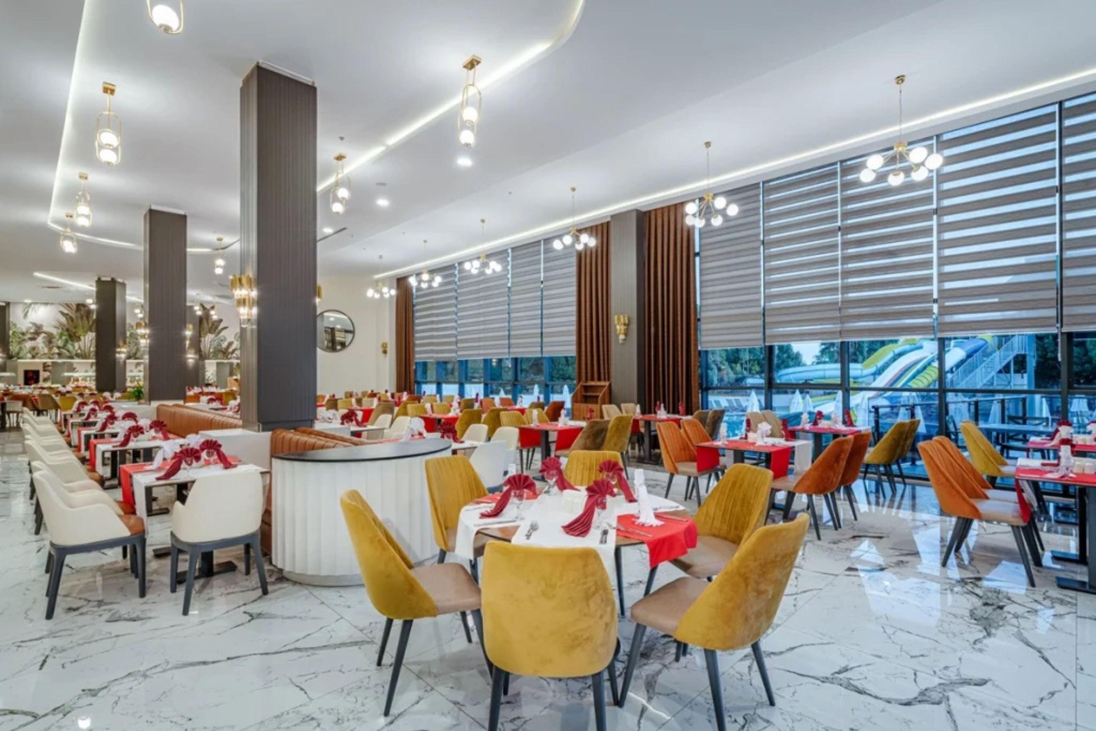 Un restaurant spacieux avec de hauts plafonds, un éclairage moderne et une vue sur un parc aquatique avec des toboggans situé à l’extérieur.