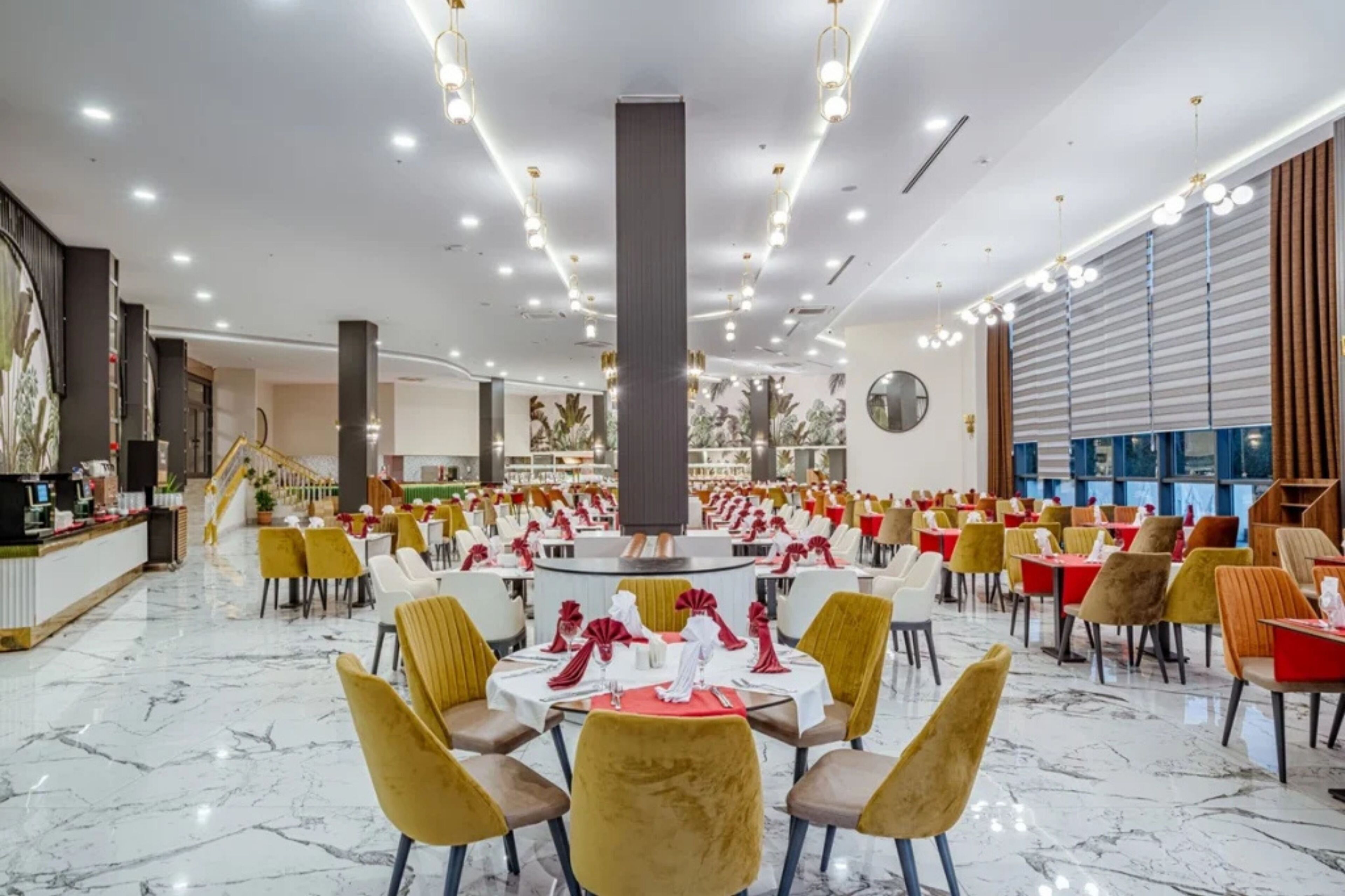 Un comedor amplio con mesas redondas, sillas amarillas y una columna central.