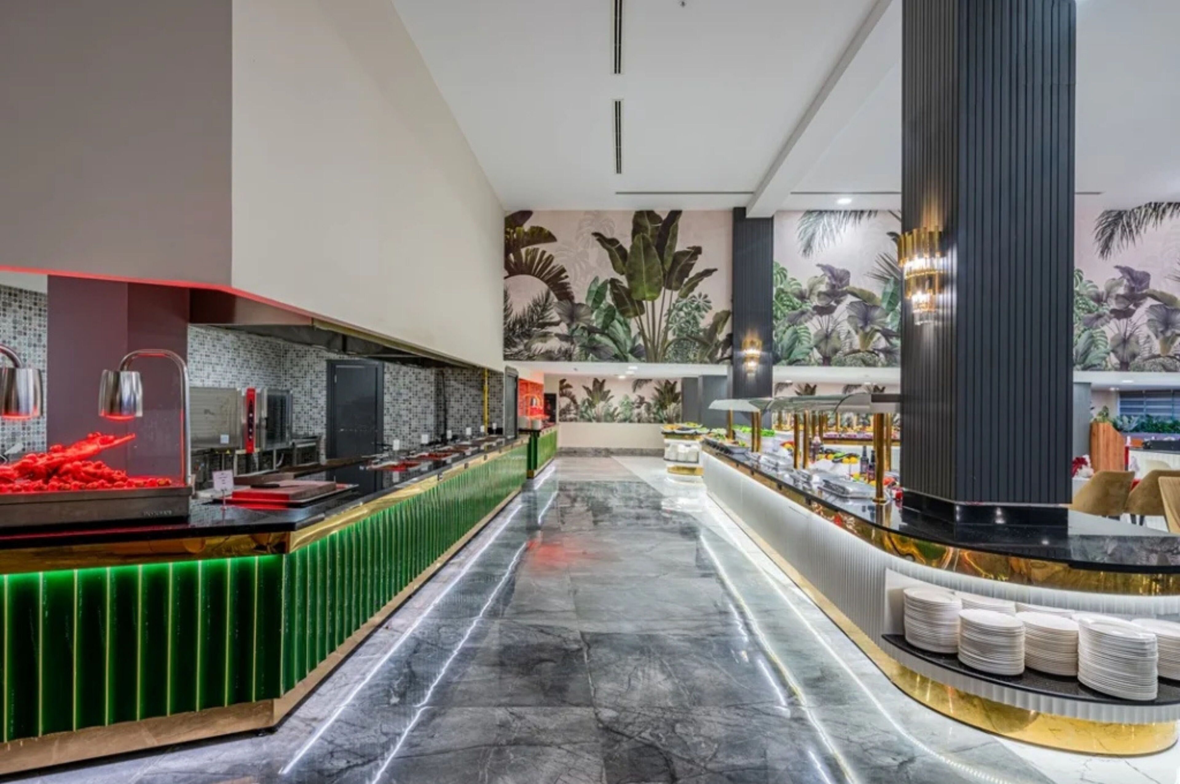 A modern hotel lobby with a long reception desk, a large mural of tropical plants, and a marble floor.