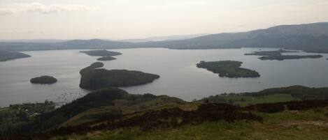 A panoramic view of a lake with multiple islands, surrounded by hills and a grassy foreground.