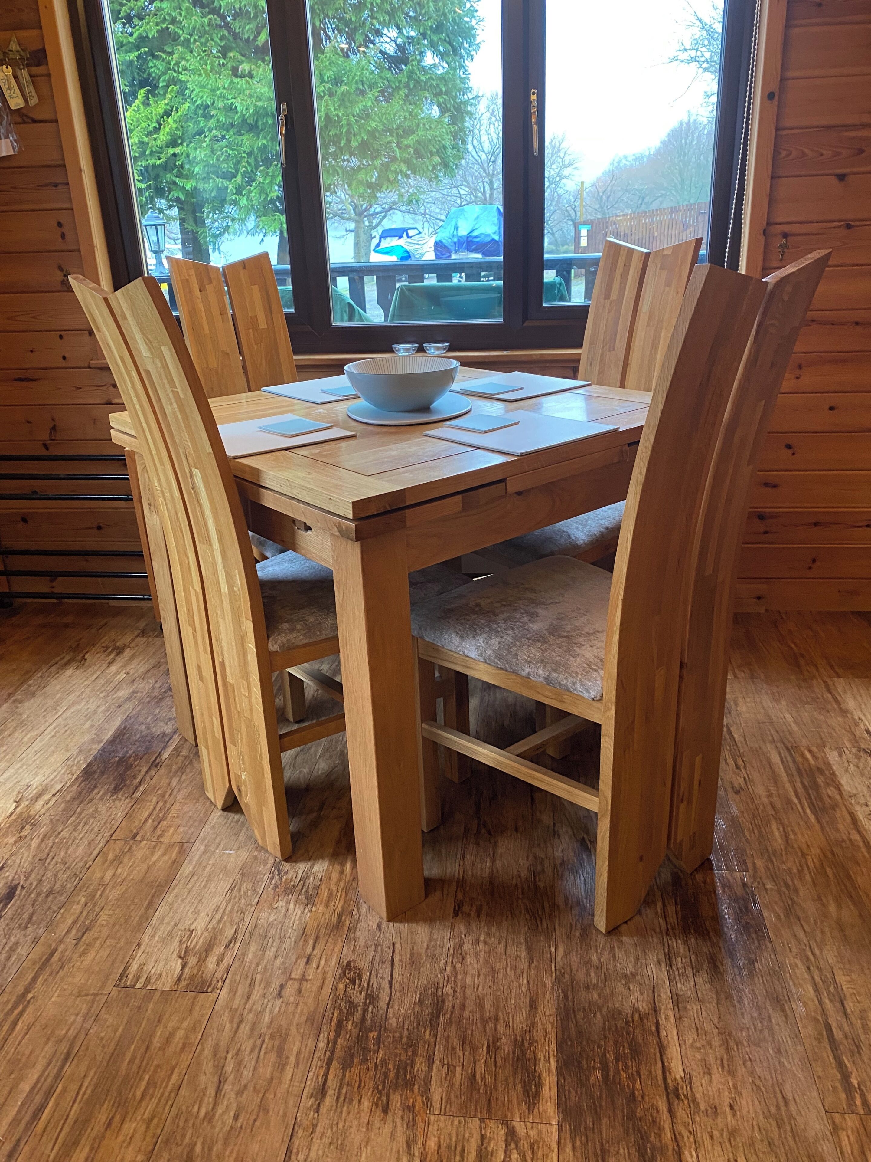Une table à manger en bois, avec des chaises, un saladier et des sets de table.