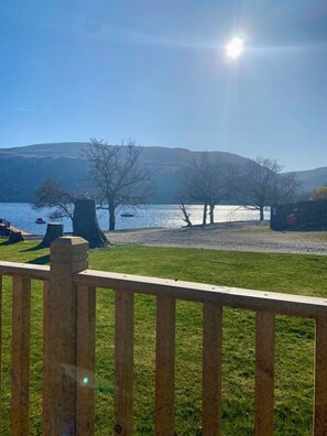 A grassy area with a wooden fence, trees, and a body of water with boats. - Loch Lomond Lodge 27, Rowardennan (Rowardennan)