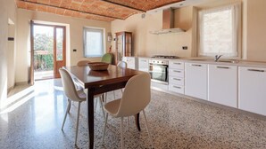 Una cocina con techo de ladrillo, armarios blancos, una mesa de comedor con sillas y una ventana.