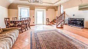 Amplia sala de estar con mesa de comedor, sillas, sofá, televisor y una escalera.