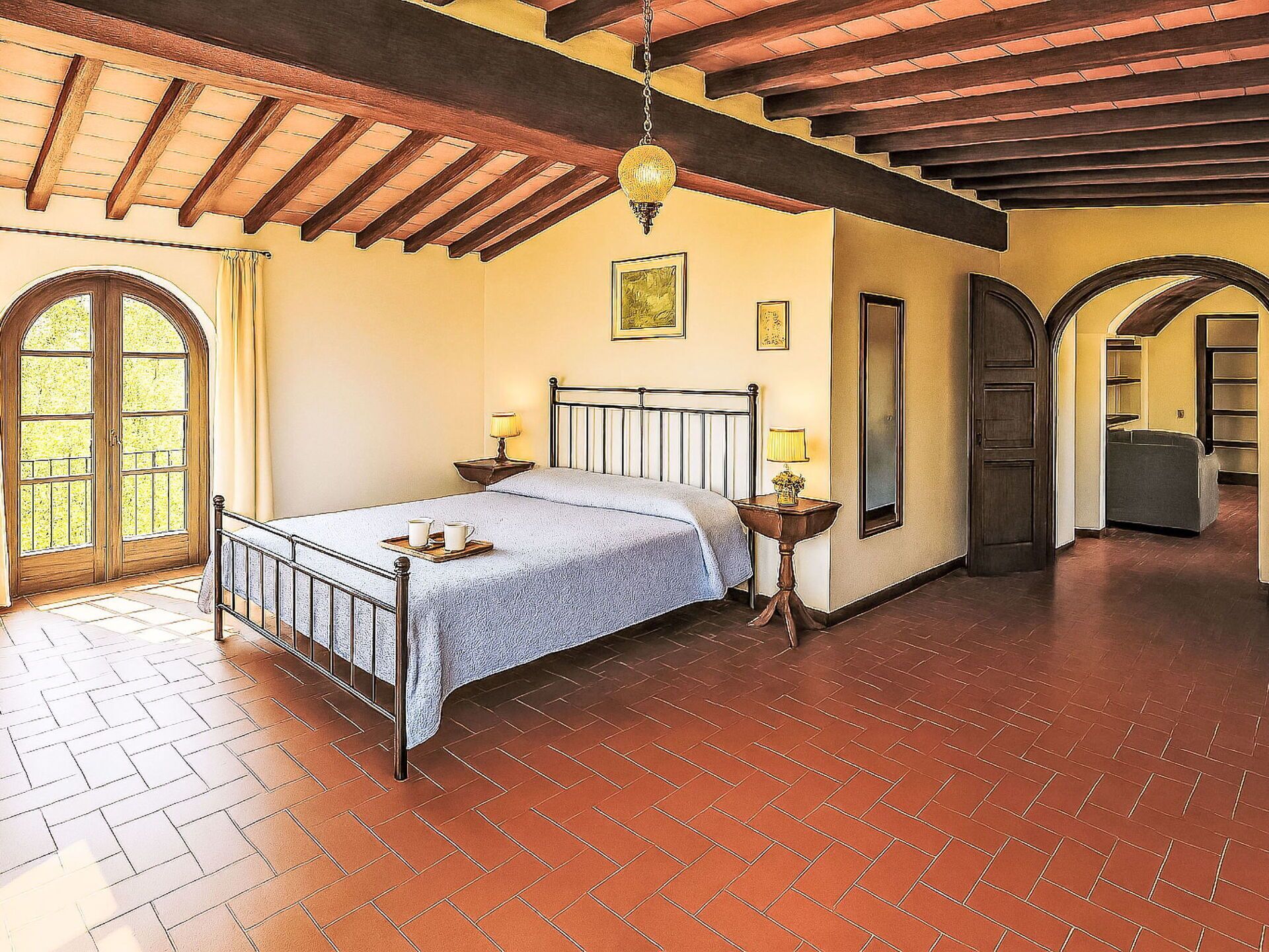 Un dormitorio con cama, mesitas de noche, lámpara colgante y un ventanal grande.