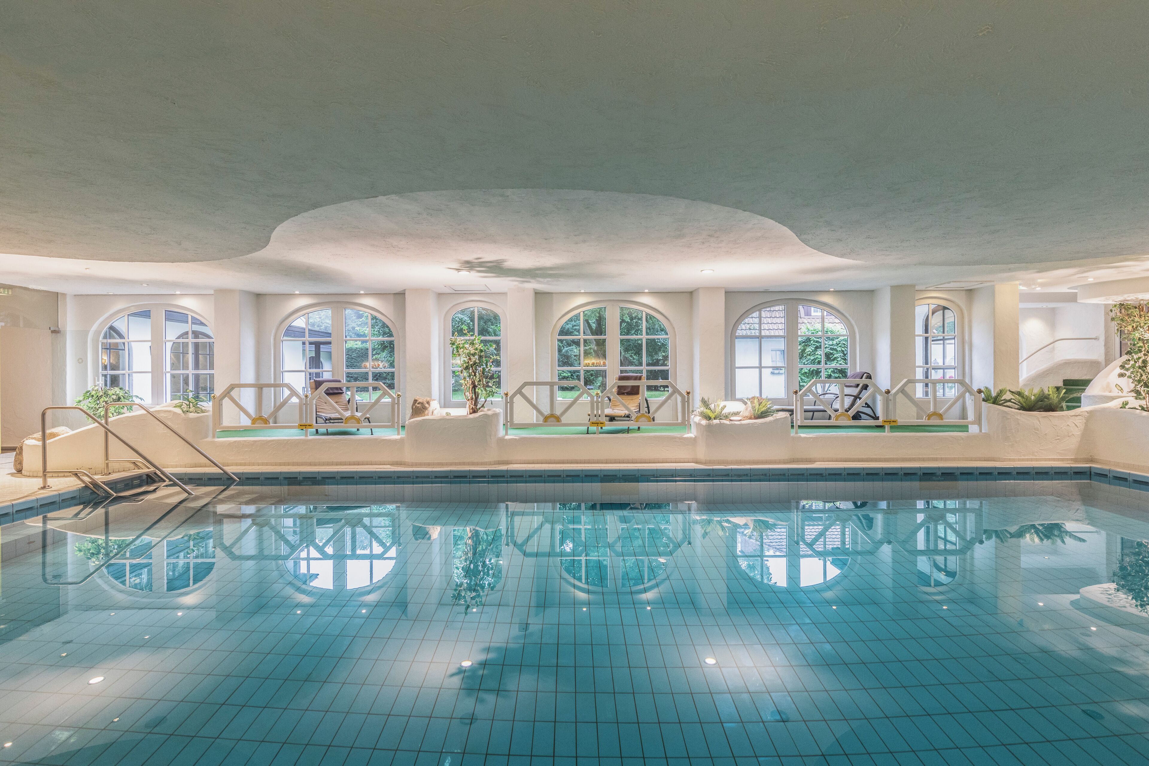 An indoor swimming pool with arched windows and a tiled floor.