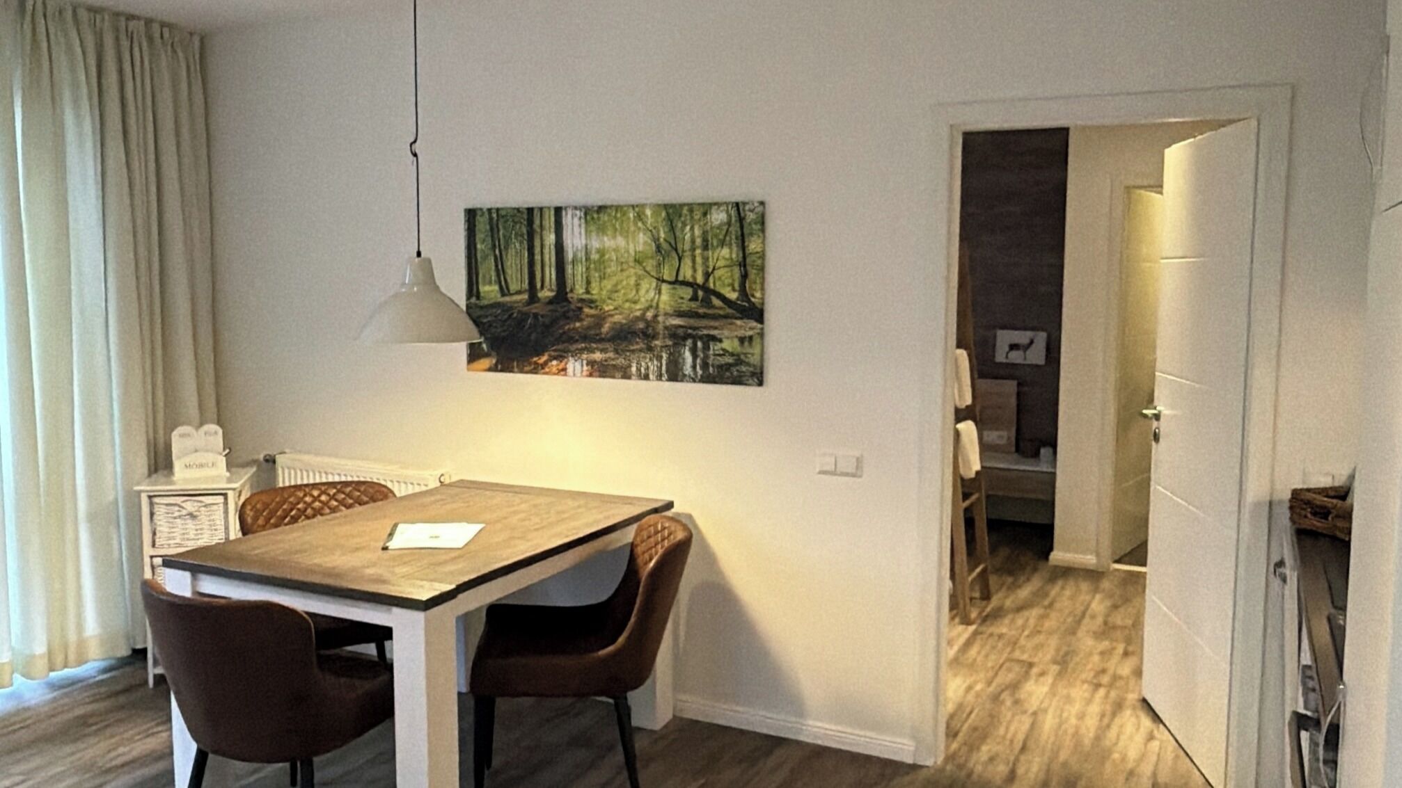 A dining area with a table and chairs, a pendant light, and a painting on the wall.