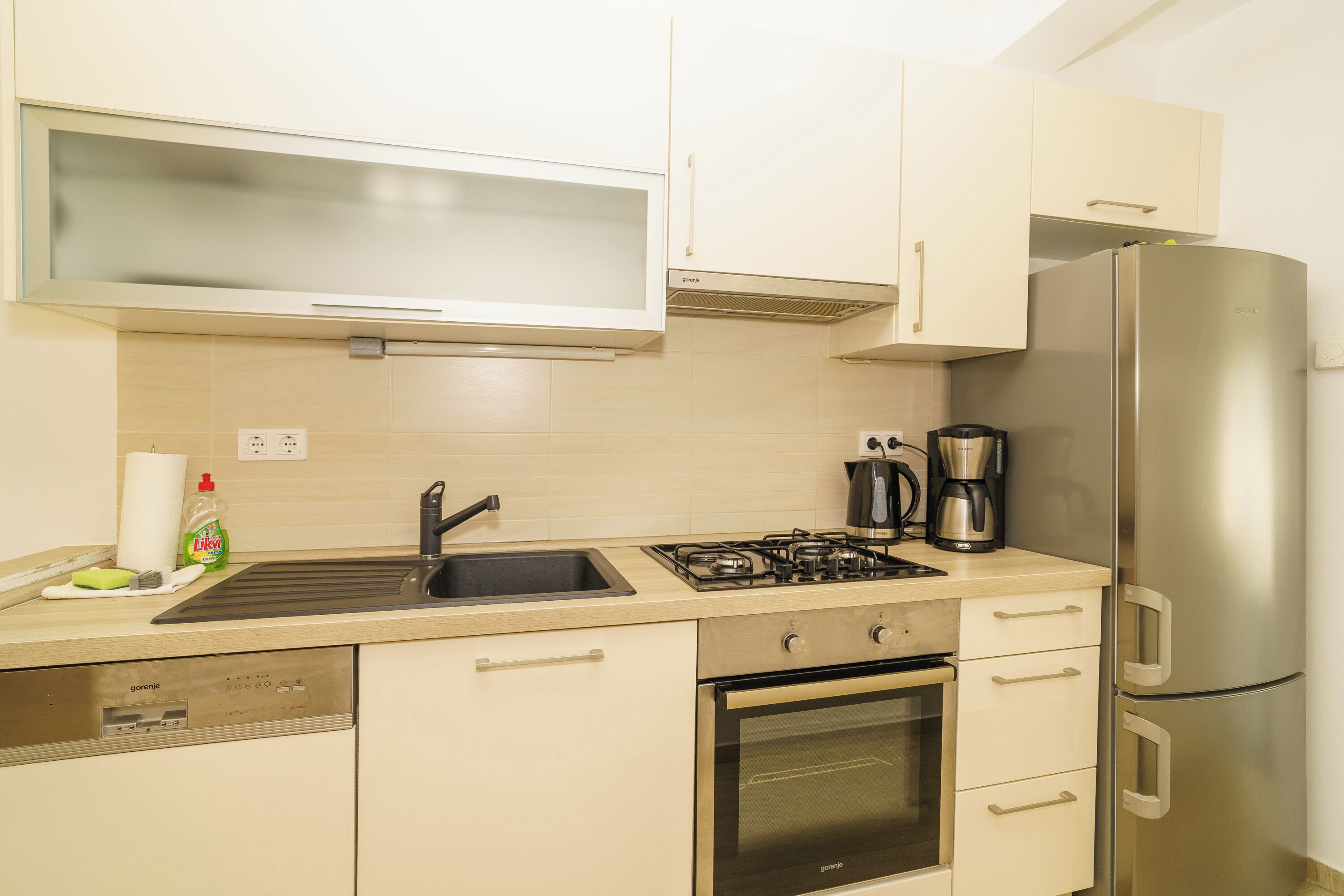 A modern kitchen with a dishwasher, oven, stove, sink, and a stainless steel refrigerator.