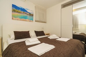 A hotel room with a bed, a painting of a coastal scene, a mirror, and a window with curtains. - Beachfront apartment in Crikvenica with barbecue & garden (Crikvenica)