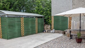 Un'area patio coperta con pavimento in cemento, capienti casette portaoggetti verdi e una panchina in legno.