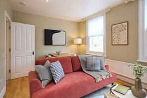 Ein Wohnzimmer mit einem roten Sofa, einer Lampe und Kunstwerken an der Wand.