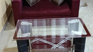 Ein rotes Sofa mit zwei dunklen Kissen und einem Glastisch mit Metallbeinen.