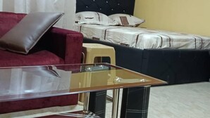 Ein Hotelzimmer mit Glastisch, rotem Sofa, Bett mit weißer Bettwäsche und gelber Wand.