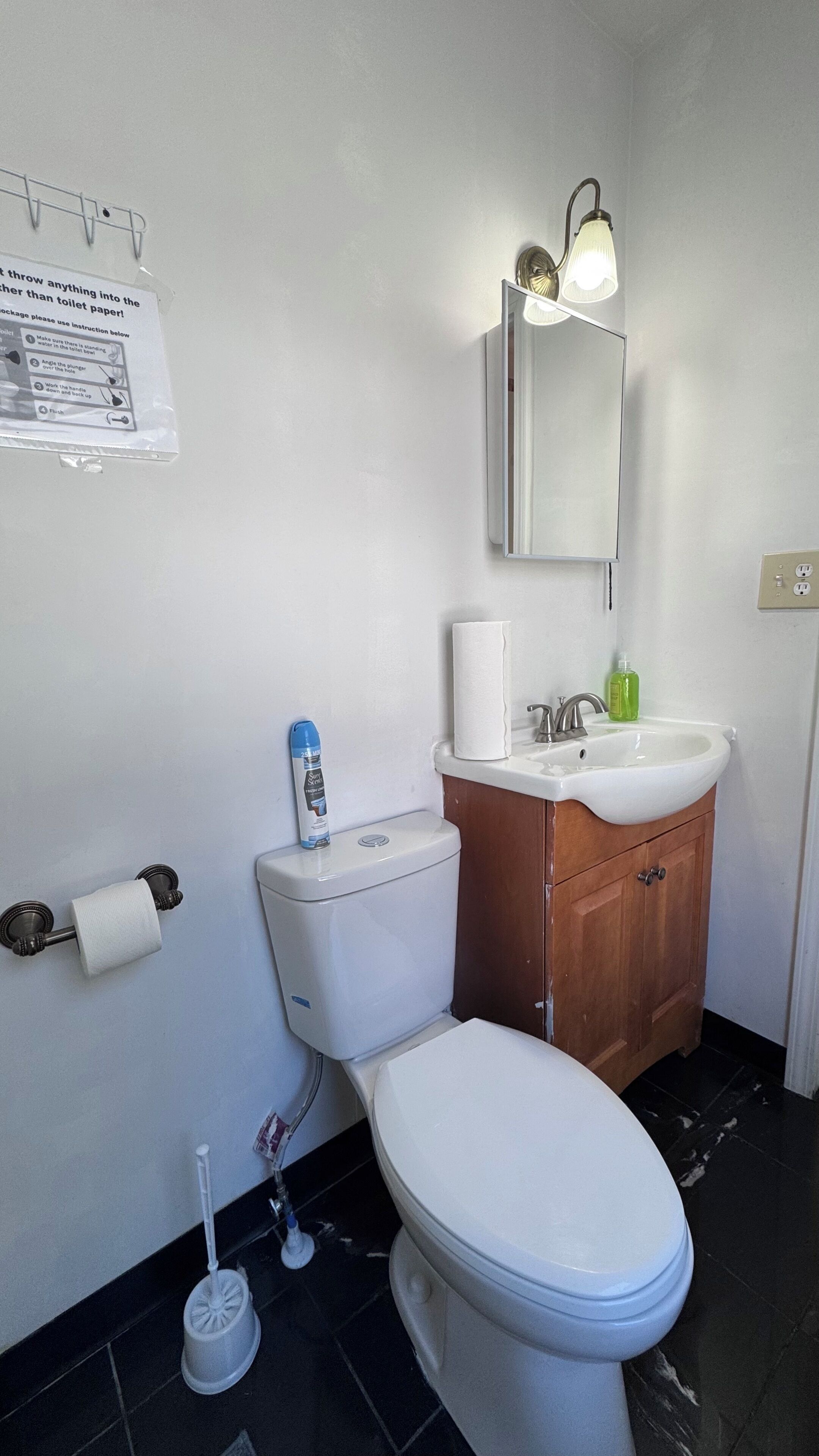 A bathroom with a toilet, sink, mirror, and a paper towel dispenser.