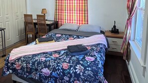 Ein Schlafzimmer mit einem Bett, einem Schreibtisch, Stühlen, einem Deckenventilator und einem Fenster mit Vorhängen.