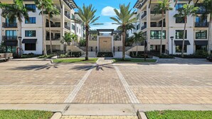 Un immeuble résidentiel moderne à plusieurs étages, doté de balcons, d’une entrée principale et de palmiers.