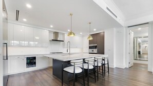 Une cuisine moderne avec des meubles blancs, un îlot central doté de tabourets et des luminaires suspendus.