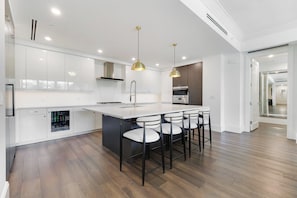A modern kitchen with white cabinetry, a central island with bar stools, and pendant lighting. - Quattro at Naples Square (Naples)