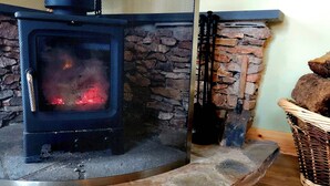 A wood-burning stove with a stone facade, a metal mesh front, and a chimney. - Cabin View (Turriff)