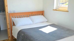 A single bed with a wooden frame, white bedding, and a grey blanket. - Cabin View (Turriff)