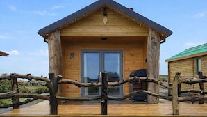 A wooden cabin with a deck, a large sliding door, and a small porch area. - Cabin View (Turriff)