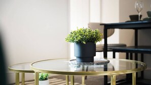 A round glass table with a black planter on top, a gold-framed chair, and a sofa in the background. - Modern 4BR with Easy Access to Town and Station (Darlington)