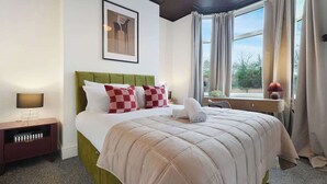 A neatly made bed with a green headboard, a bedside table with a lamp, and a window with curtains. - Modern 4BR with Easy Access to Town and Station (Darlington)