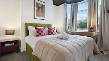 A neatly made bed with a green headboard, a bedside table with a lamp, and a window with curtains.
